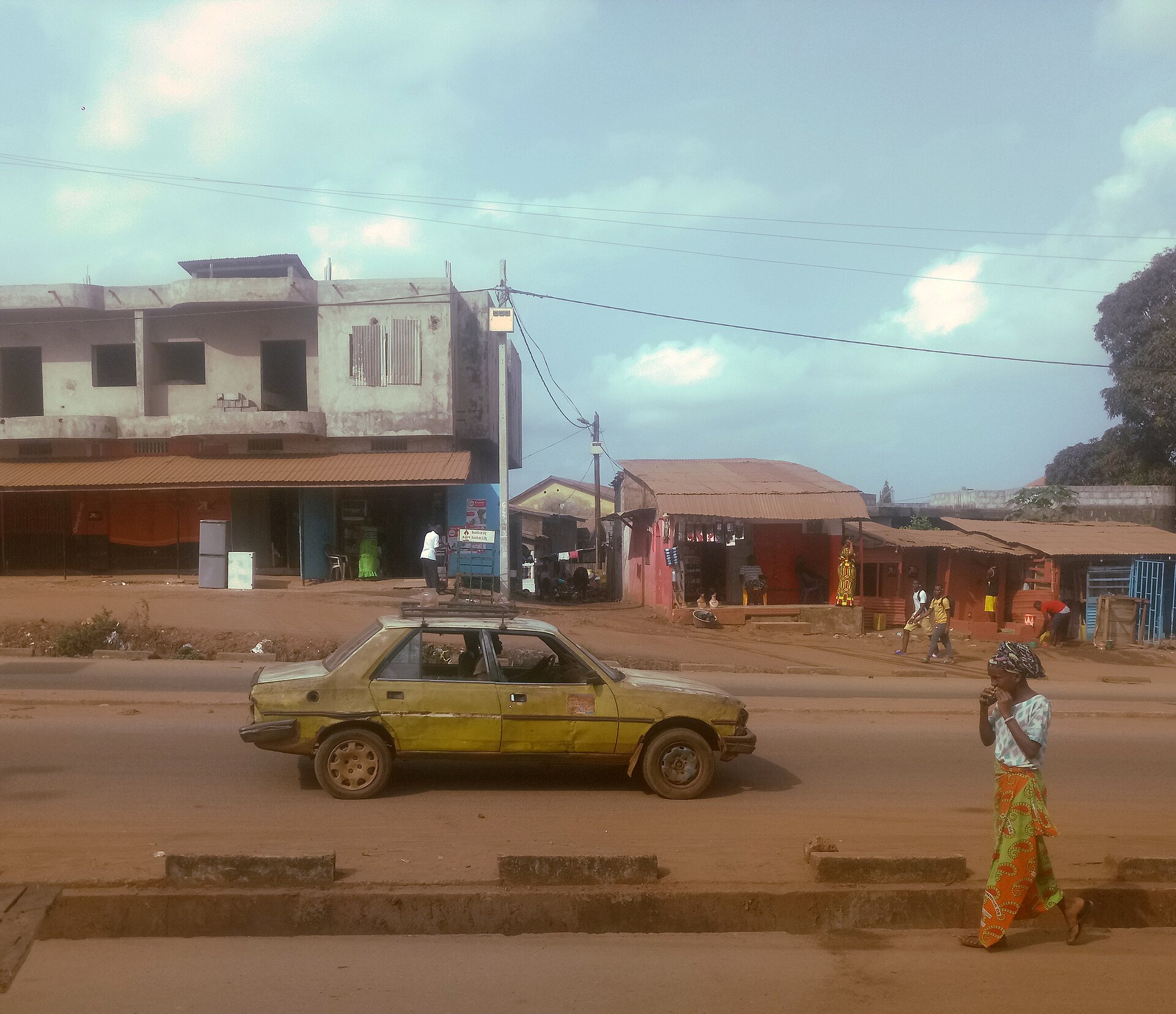 A taxi passing shopfronts on a road in Conakry